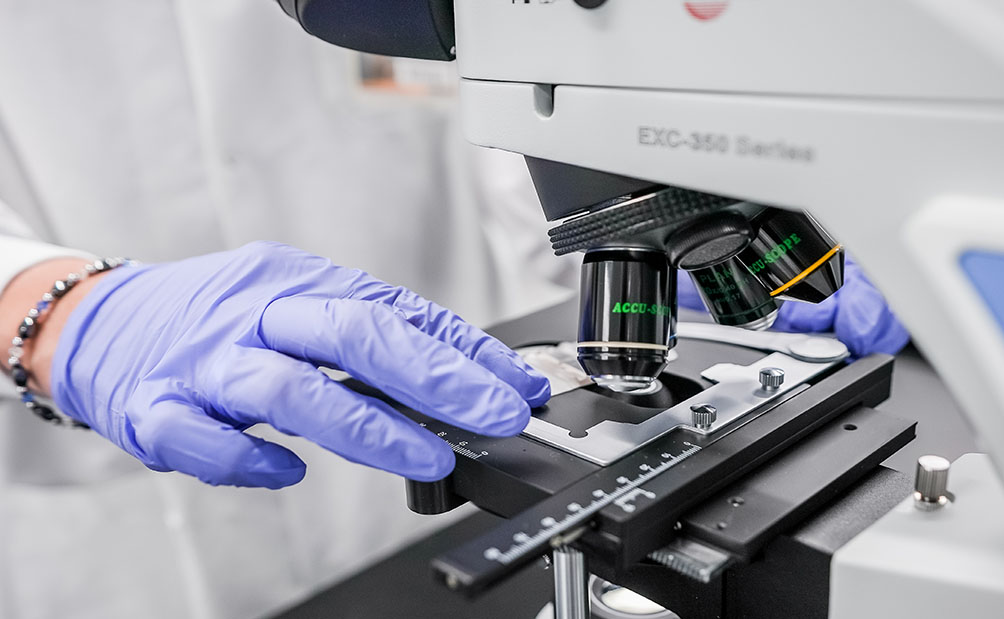Cell therapy scientist wearing gloves handling a microscope.